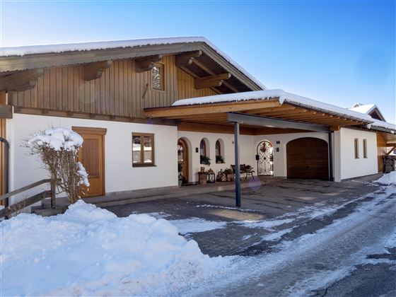 A modern house in the snow with wood siding and garage space. The surroundings are wintry and inviting.