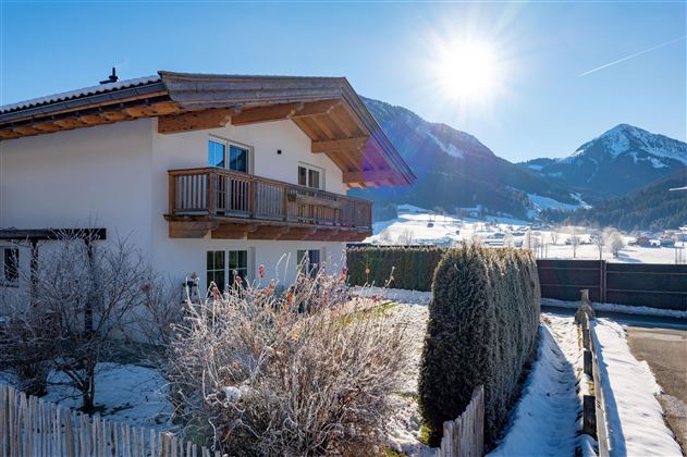 Ein schönes Haus in den Bergen mit einem großen Balkon. Umgeben von Schnee und einer klaren Winterlandschaft.