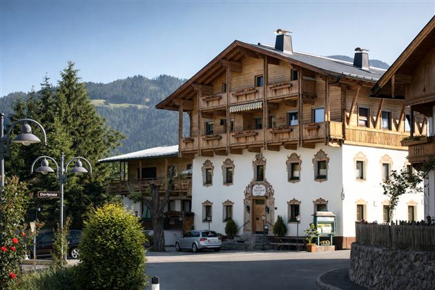 Een traditioneel houten huis in de Alpen met meerdere balkons. Omringd door bomen en een prachtig berglandschap.