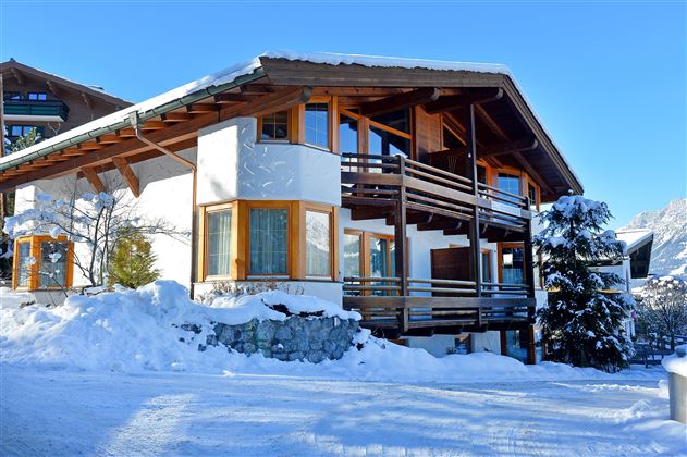 Ein gemütliches Chalet in den Bergen, umgeben von Schnee. Der klare Himmel und die sonnige Atmosphäre schaffen eine einladende Winterlandschaft.