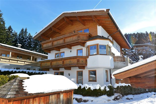 Ein modernes Chalet in den Bergen, umgeben von Schnee. Die Architektur vereint Holz und Putz mit großen Fenstern für viel Licht.