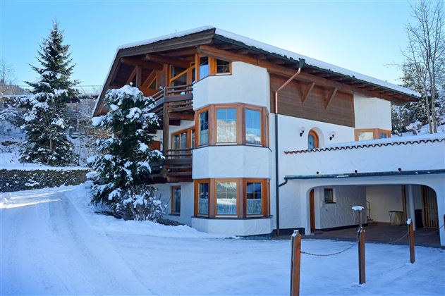 Ein modernes Haus im Schnee, umgeben von Nadelbäumen. Die große Fensterfront lässt viel Licht herein.