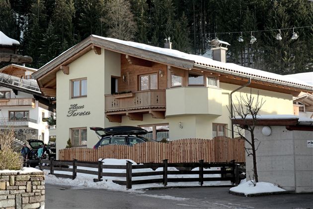 Ein gemütliches Haus im alpinen Stil mit Holzverkleidung und einem Balkon. Der Schnee und die umgebenden Bäume schaffen eine winterliche Atmosphäre.