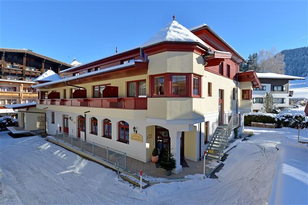A charming building in winter with snow on the roof. Surrounded by snowy hills and blue sky.