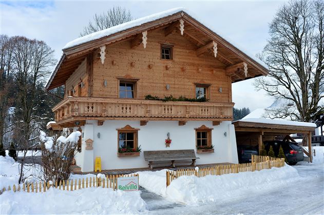 Ein schönes Holzhaus im Alpenstil, umgeben von schneebedeckter Landschaft. Es hat einen Balkon und eine gemütliche Atmosphäre.