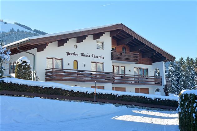 Ein charmantes Haus im alpinen Stil, umgeben von Schnee. Es hat einen großen Balkon und ist von malerischen Bergen umgeben.