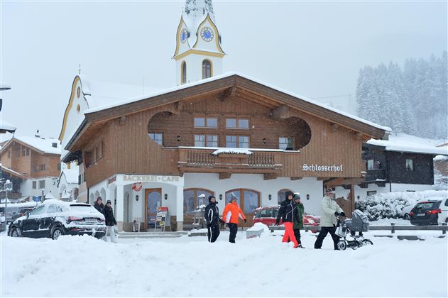 A traditional wooden house in the snow with a clock tower. People walk by and enjoy the winter landscape.