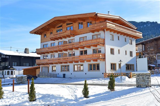 A modern building in alpine style, surrounded by snow. The facade is made of wood and is brightly painted.