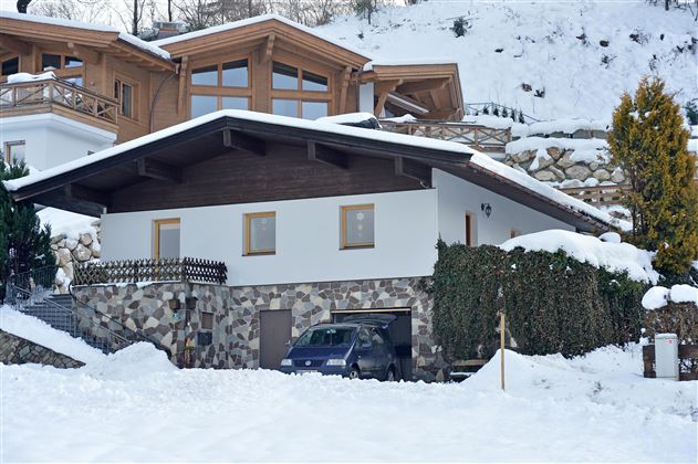 A house in the snow with a stone foundation and a modern roof. Fresh snow is everywhere, and there are some green bushes.