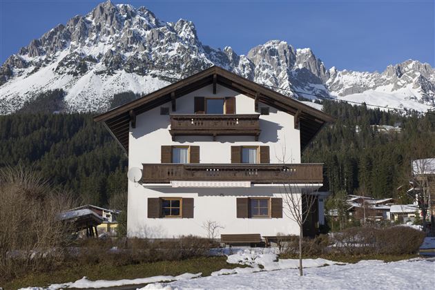 A charming house surrounded by snow-covered mountains. The clear blue sky gives the scene a calm atmosphere.