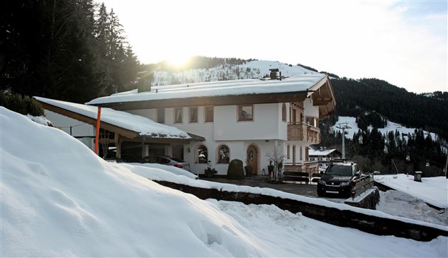 A charming chalet in the snow with mountains in the background. The sun gently shines on the building and the surroundings.