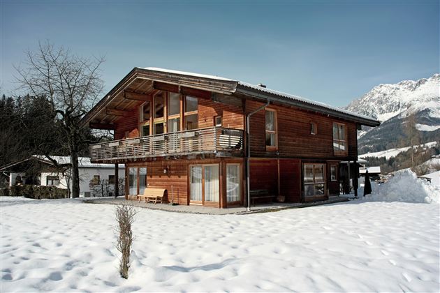 Een mooi houten huis in een besneeuwd landschap. Op de achtergrond zijn bergen te zien.