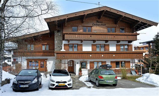 Ein traditionelles Chalet im alpinen Stil mit Holzverkleidung. Vor dem Gebäude stehen mehrere Autos und die Umgebung ist schneebedeckt.