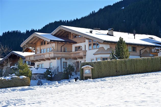 A beautiful, snow-covered building in the mountains. Surrounded by trees and a clear sky.