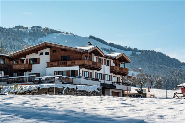 Ein schönes, schneebedecktes Haus in den Bergen. Im Hintergrund sind schneebedeckte Hügel und ein klarer blauer Himmel zu sehen.