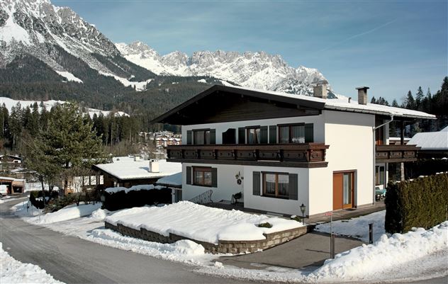 Ein modernes Haus in den Bergen, umgeben von Schnee. Die majestätischen Gipfel sind im Hintergrund zu sehen.