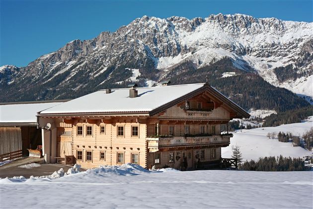 Ein charmantes Holzhhaus im Schnee mit beeindruckenden Bergen im Hintergrund. Die Landschaft ist winterlich und ruhig.