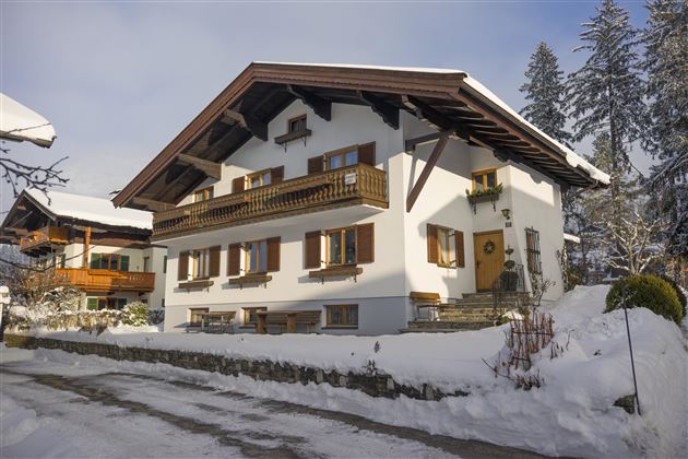 A traditional house in the snow with a balcony and wooden windows. The surroundings are wintry and peaceful.