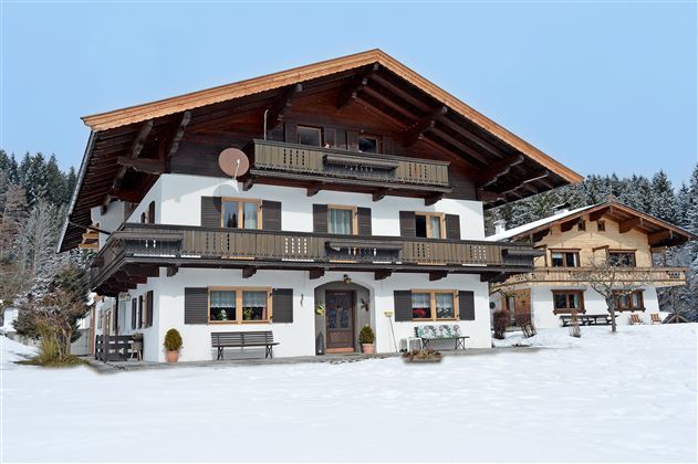 A large, rustic chalet in the snow, surrounded by a wintry landscape. The sky is clear and the surroundings are peaceful.