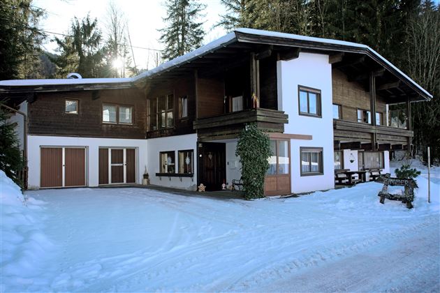 A large house in the snow, surrounded by tall trees. The architecture combines modern and traditional elements.