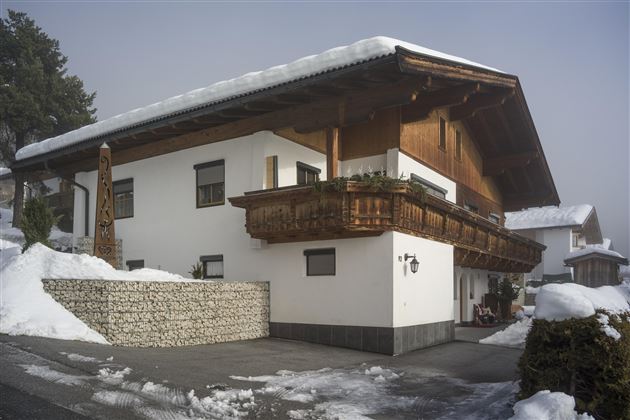 A cozy chalet in the snow with a traditional wooden balcony. The surroundings are wintry and peaceful.