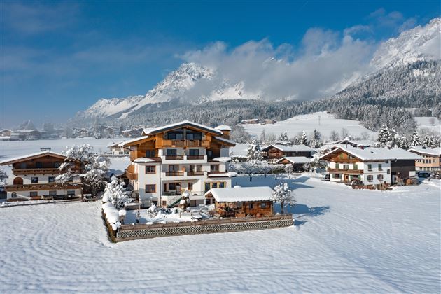 Eine malerische Winterlandschaft mit schneebedeckten Häusern und Bergen im Hintergrund. Der Himmel ist klar und blau, was die Szene besonders einladend macht.