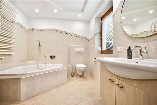 Ein modernes Badezimmer mit einer Badewanne, einem Waschbecken und einer Toilette. Die Wände sind in neutralen Farben gehalten und es gibt einen großen Spiegel.