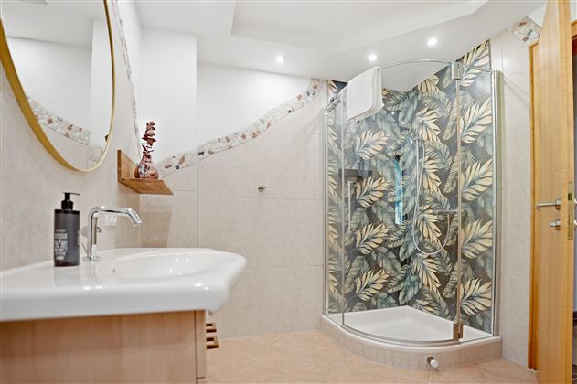 Ein modernes Badezimmer mit einer Dusche und blattartigen Wandtapeten. Der Waschbeckenbereich ist hell und einladend gestaltet.