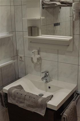 A modern bathroom with a sink and a mirror. Towels and toiletries are arranged on the shelves.