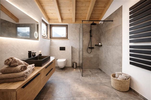 Ein modernes Badezimmer mit Holzdecke und eleganten Fliesen. Es enthält eine begehbare Dusche, ein Waschbecken und eine gemütliche Atmosphäre.