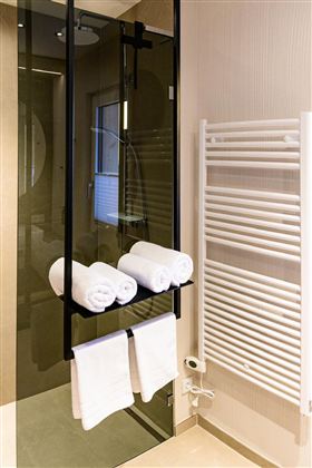 A modern bathroom with a glass shower and a towel rack. White towels are neatly lined up.