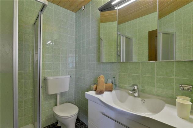 A modern bathroom with green tiles and a large mirror. The fixtures include a shower, a sink, and a toilet.