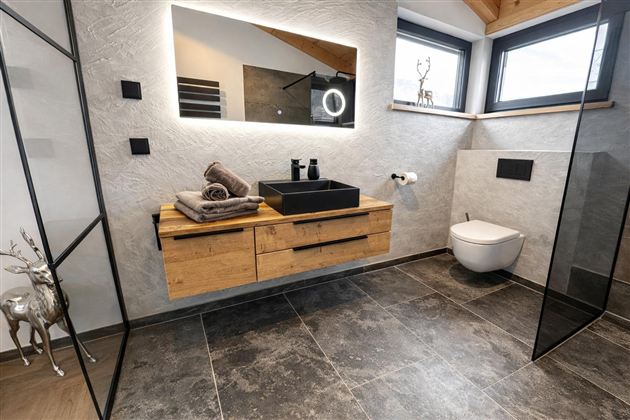 Ein modernes Badezimmer mit einer eleganten Holzwaschtischplatte und einem großen Spiegel. Die Wände sind neutral gehalten, und es gibt große Fenster, die viel Licht hereinlassen.