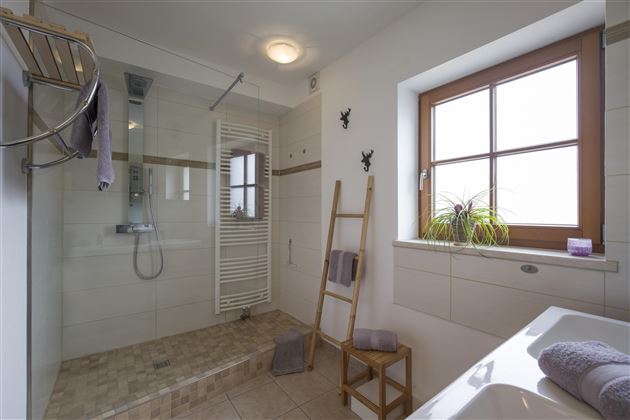 Ein modernes Badezimmer mit einer Dusche und einer Badewanne. Große Fenster sorgen für viel Tageslicht und eine angenehme Atmosphäre.