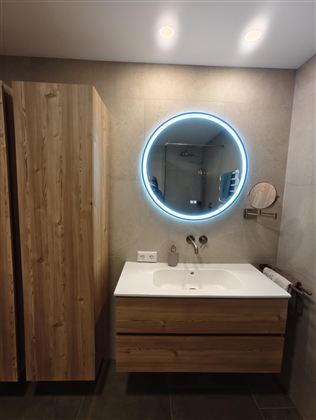 A modern bathroom with wooden cabinets and an elegant sink. An illuminated round mirror complements the stylish design.