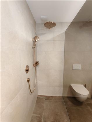 A modern bathroom with an elegant shower and golden fittings. The walls are tiled in light tones, creating a calming atmosphere.