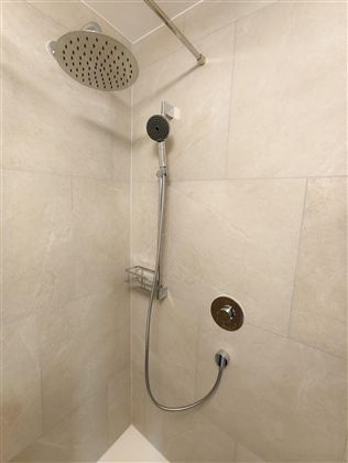 Een moderne douche met een grote regendouche en een handdouche. De wanden zijn voorzien van lichte tegels.