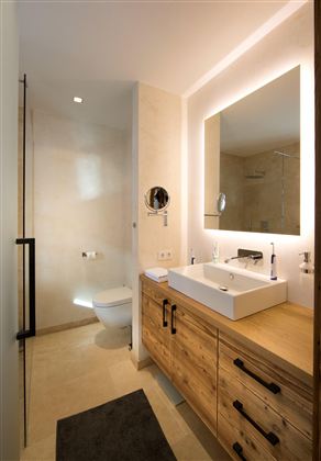 Ein modernes Badezimmer mit Holzschränken und einem eleganten Waschbecken. Die Dusche ist durch Glaswände abgetrennt, und es gibt eine große Spiegelwand.