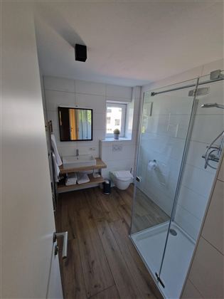 Ein modernes Badezimmer mit einer Dusche und einem WC. Es gibt einen Spiegel und eine kleine Ablage mit Handtüchern.