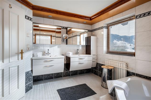 Ein modernes Badezimmer mit einer begehbaren Dusche und hellen Fliesen. Es gibt Pflanzen und Handtücher in roten Farben.