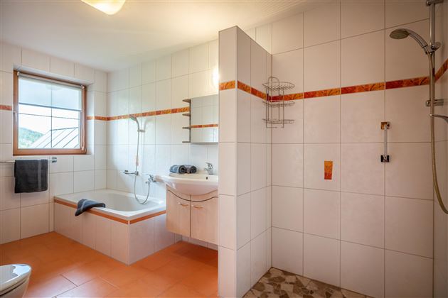A bright bathroom with a bathtub and a shower. The walls are tiled, and there is a window that lets in light.