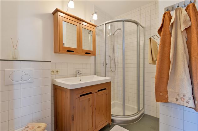 A modern bathroom with a shower and a wooden washbasin. The walls are tiled and there are two mirror pieces above the washbasin.
