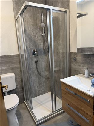 Ein modernes Badezimmer mit einer Glasdusche und Holzwaschtisch. Die Wände sind in neutralen Grautönen gehalten.