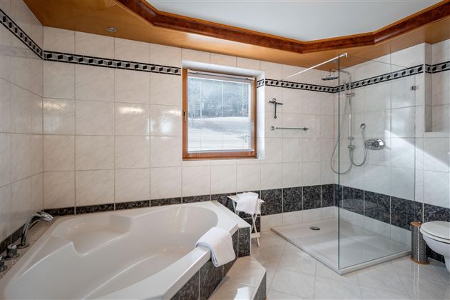 Eine moderne Dusche mit einer glatten weißen Wand und einer Duschvorhang mit Waldmotiv. Der Boden ist dunkel und der Raum wirkt hell und sauber.