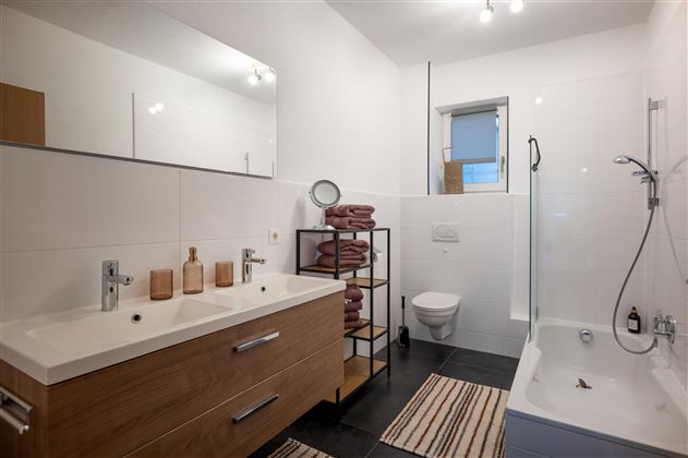 Ein modernes Badezimmer mit einer Duschkabine und einer Badewanne. Es gibt einen Doppelwaschtisch und handtuchlagernde Regale.