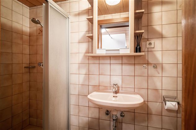 Ein kleines Badezimmer mit einer Dusche und einem Waschbecken. Die Wände sind gefliest und die Decke ist aus Holz.