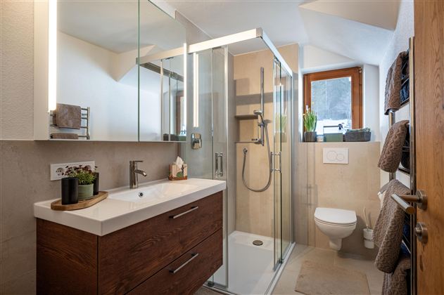 A modern bathroom with a shower and a wooden sink. Natural light falls through the window onto the bright design of the room.