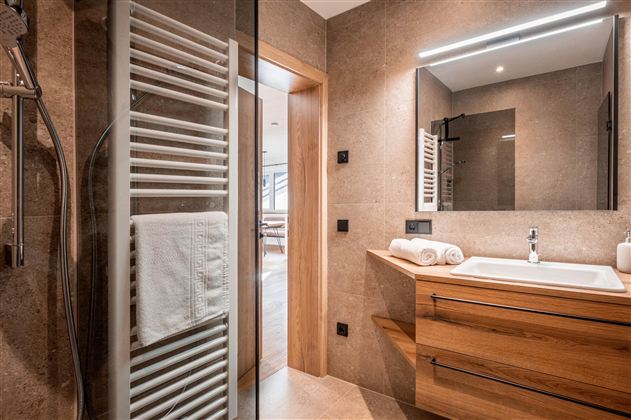 Ein modernes Badezimmer mit einer Dusche, einem Holzwaschtisch und einem Spiegel. Die Wände sind in warmen Erdtönen gehalten.