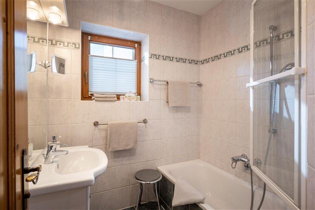 Ein modernes Badezimmer mit einer Badewanne und einer Dusche. Die Wände sind hell gefliest, und es gibt ein Fenster für natürliches Licht.