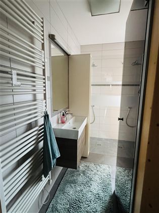 Een moderne badkamer met een douche en een wastafel. De ruimte is licht en stijlvol ingericht, met een handdoek en een deurmat in een prettige kleur.